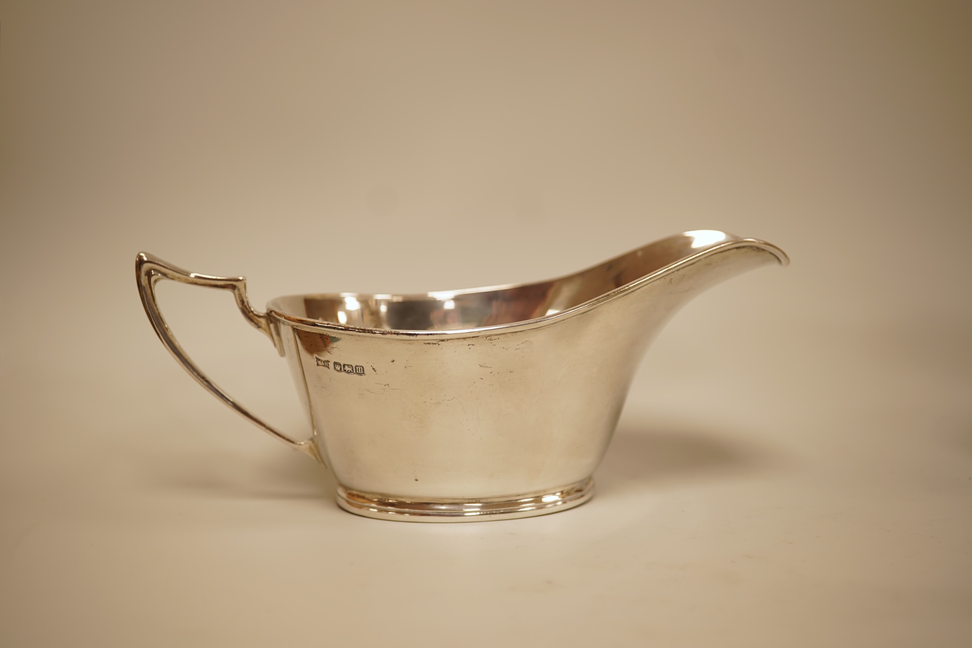A pair of George V silver sauceboats by Walker & Hall, Sheffield, 1929/30, length 17.9cm together with a George V silver sauceboat with flying scroll handle, William Comyns & Sons Ltd, London 1926, 16.4oz.